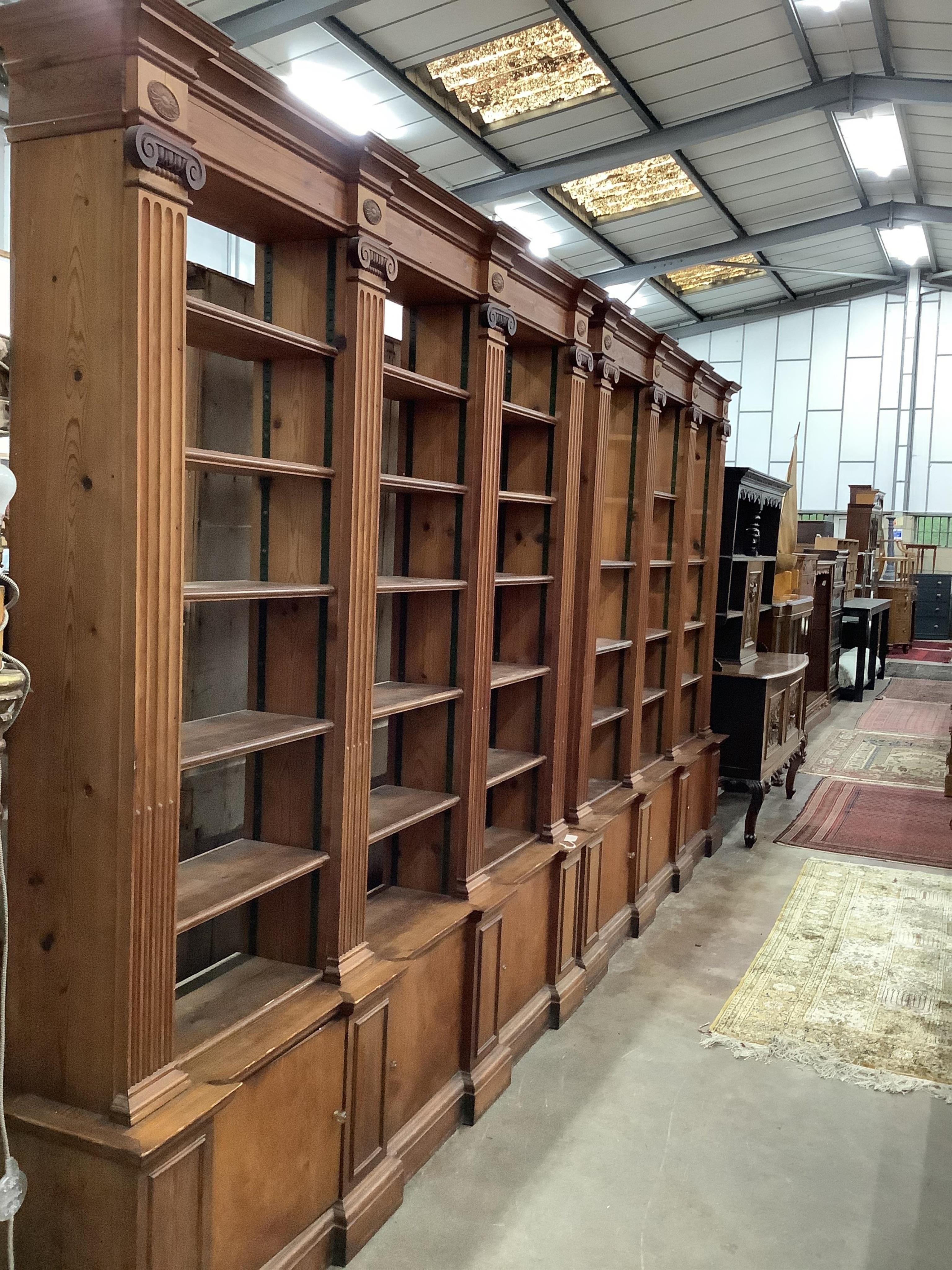 A pair of mid 20th century Sheraton style pitch pine and ply open bookcases, the adjustable shelves divided by fluted Ionic columns, each width 214cm, depth 33cm, height 222cm